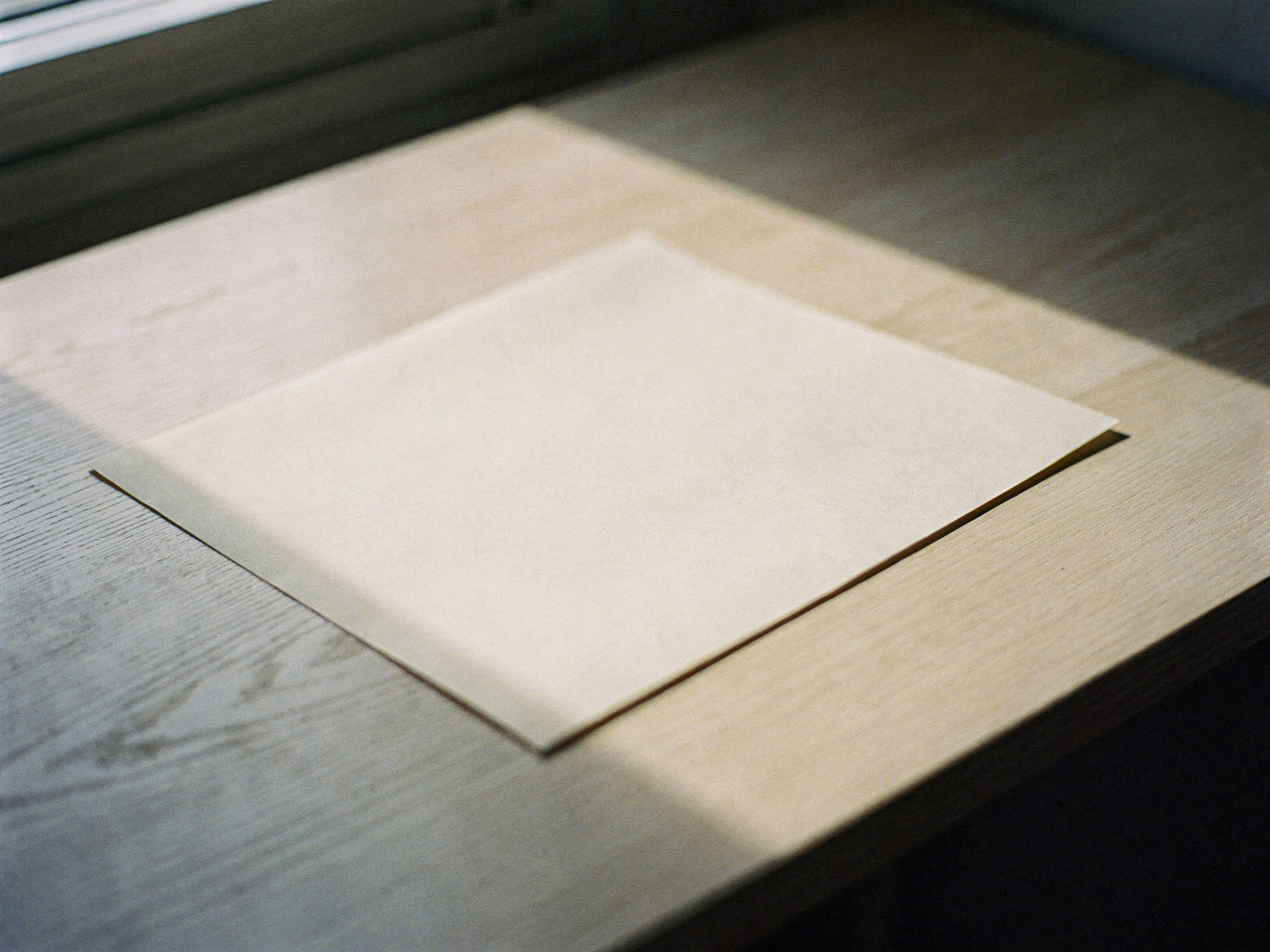 A single sheet of warm cream paper resting on a pale oak desk in soft window light